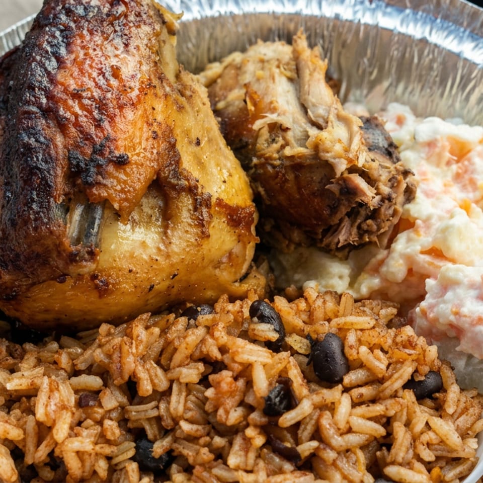 Aluminum tray filled with roasted chicken, seasoned rice and black beans, and creamy carrot potato salad.
