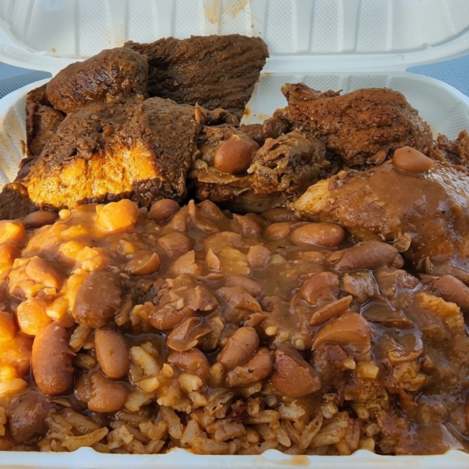 Takeout container filled with rice, beans, fried plantains, and saucy fried chicken pieces.