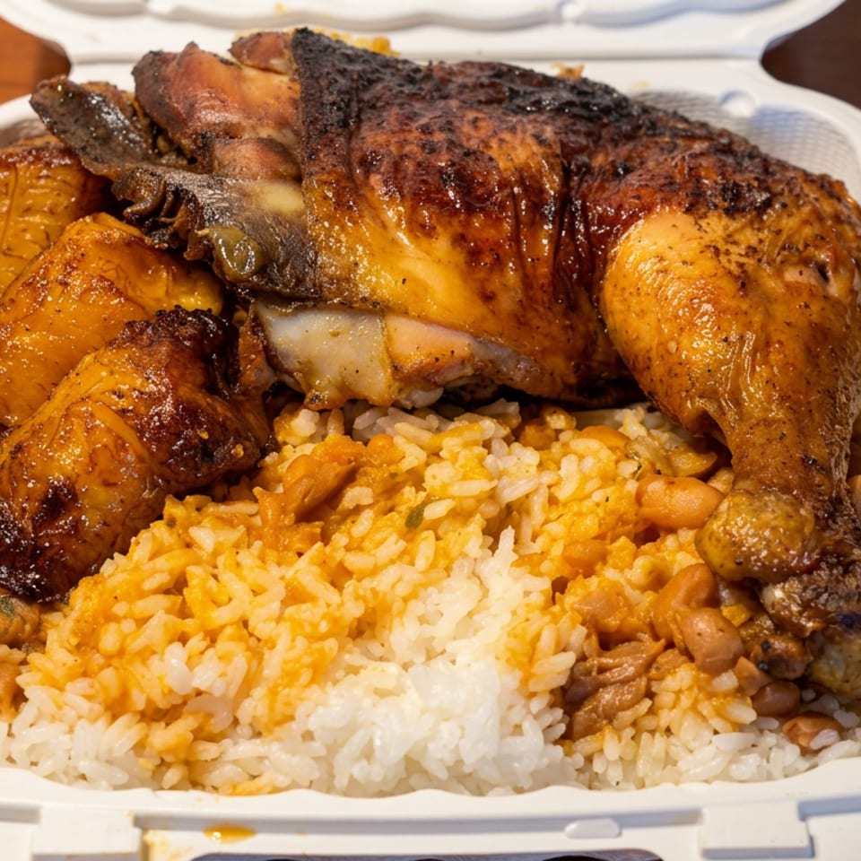 Roasted chicken pieces served over yellow rice and beans in a white takeout container on a wooden table.